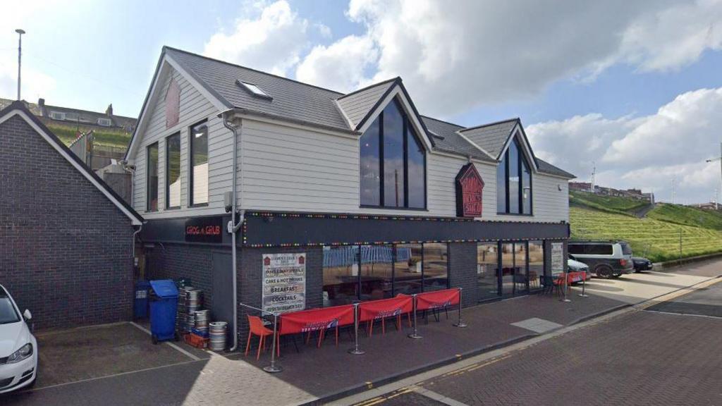 An external view of Grandpa Dickie's Shed on Marine Walk. Red chairs are placed outside the restaurant, which has large glass windows.