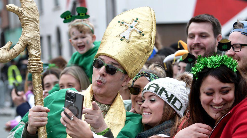 A man dressed in a costume takes photos with members of the crowd as they take part in the St. Patrick's Day parade on March 17, 2024 in Dublin, Ireland. 