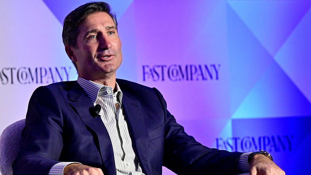 A man wearing a blue suit speaks on stage.