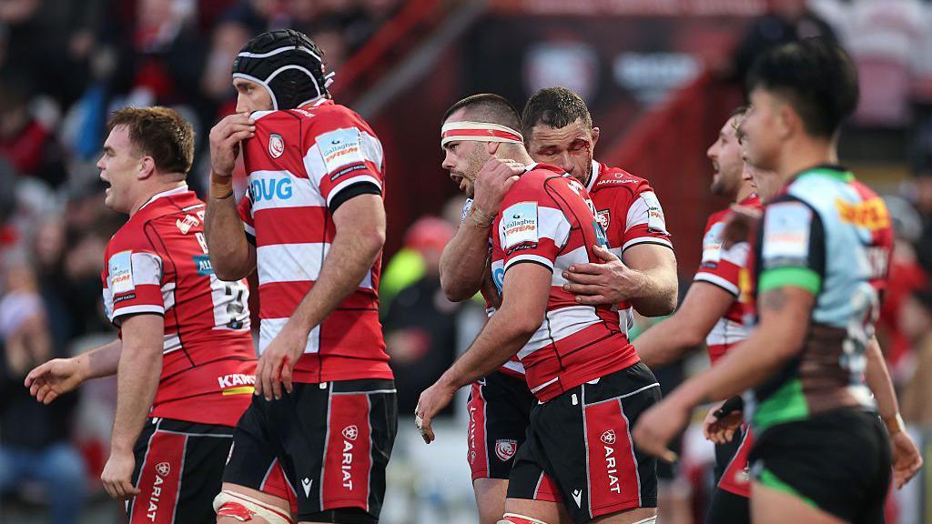 Lewis Ludlow celebrates with teammates after scoring try against Harlequins at Kingsholm. Harlequins' Marcus Smith can be seen looking on in the foreground.