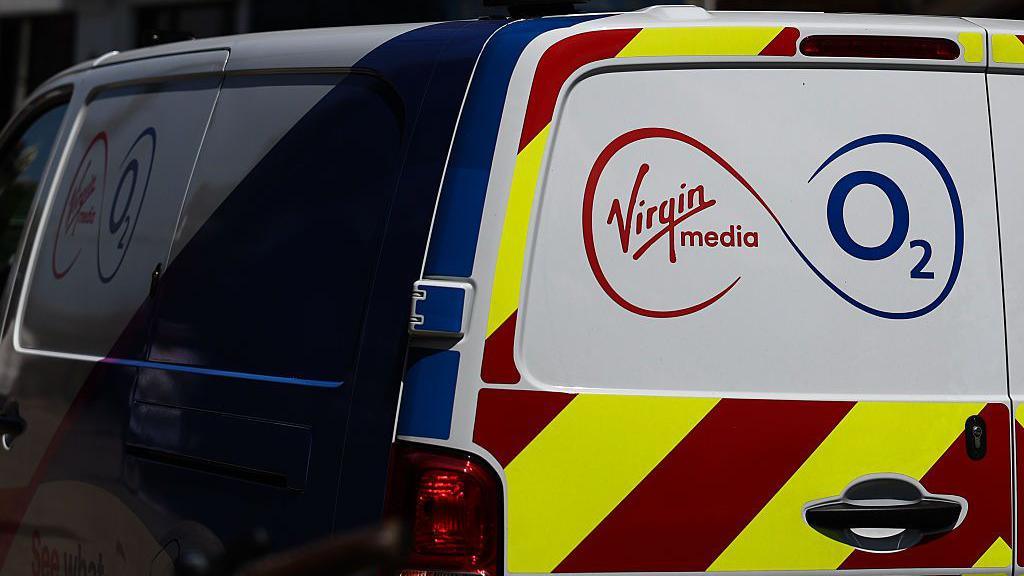 A white Virgin Media O2 van with red and yellow high-visibility stripes on the back as well as the company's red and blue logo. 