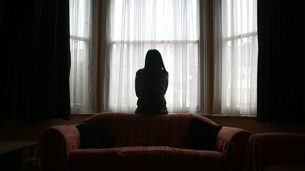 The silhouette of a woman standing alone in front of a window in a dark room