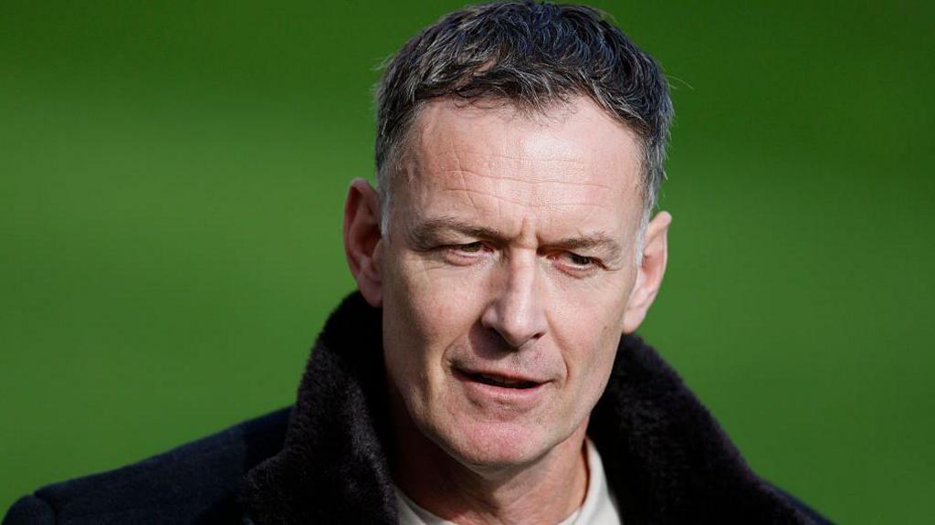 Former footballer Chris Sutton looks on from pitchside while conducting punditry at a match