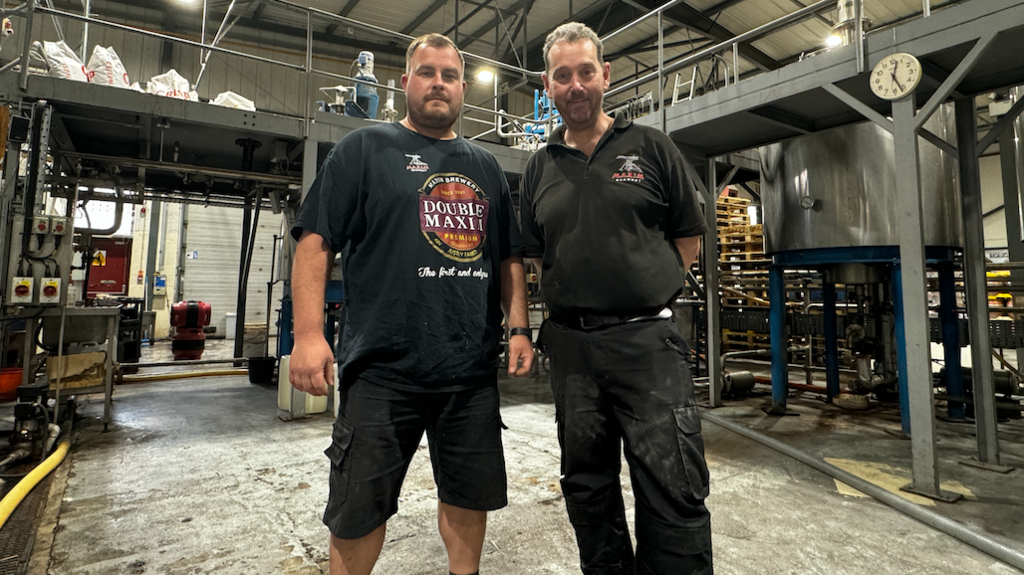 Workers stand in front of the brewery equipment inside the warehouse