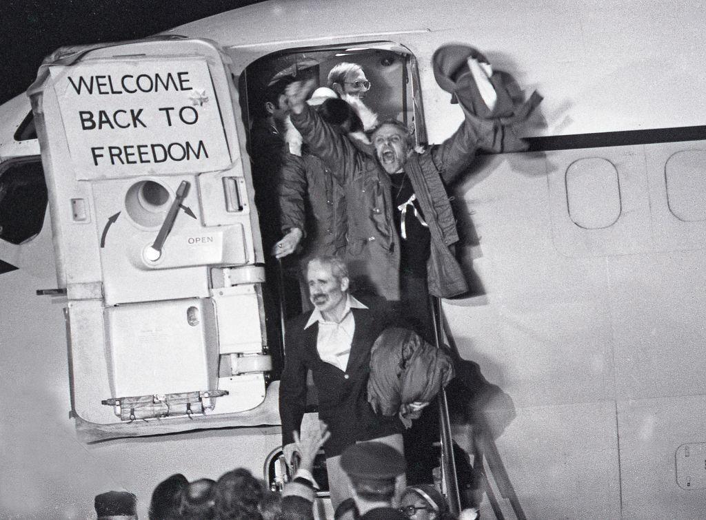 American hostages leave a plane joyously with arms in air, next to a sign that says: Welcome back to Freedom