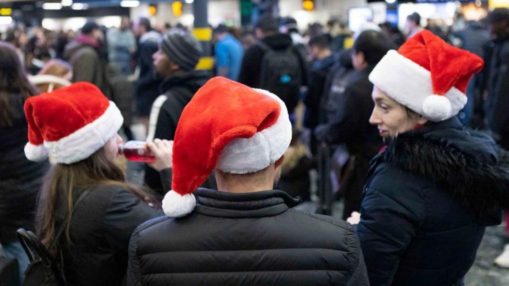 A family of three wearing black coats and Santa hats at London Euston train station