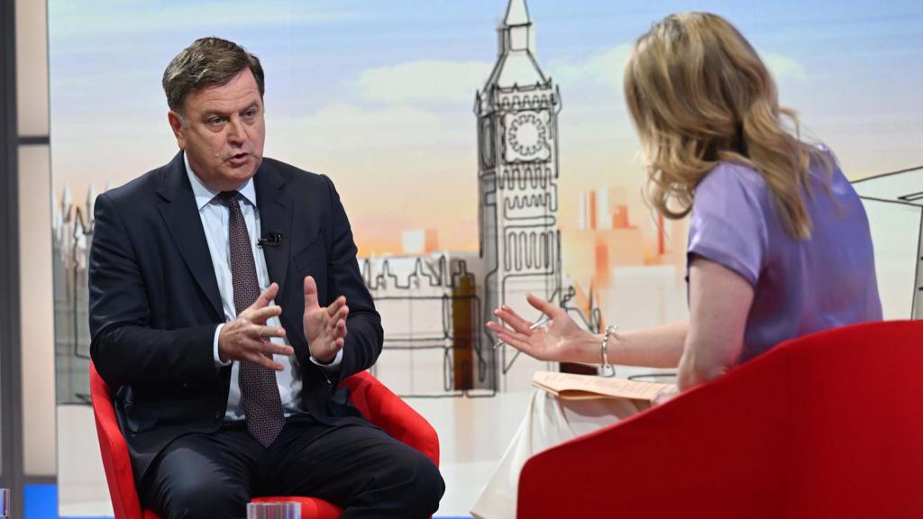 Mel Stride and Laura Keunssberg sat on red chairs speaking to each other, Laura's back to camera.