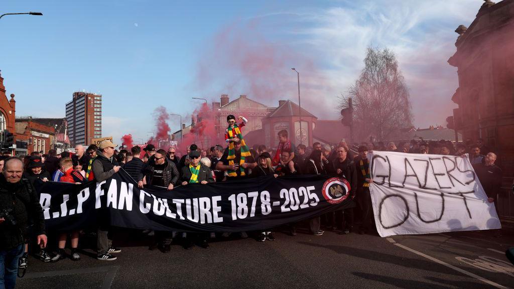  Manchester United fans protesting, holding up banners reading 'RIP fan culture 1878-2025' and 'Glazers out'