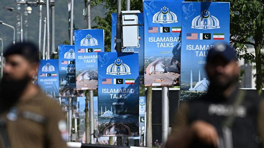 Security personnel stand guard at a security checkpost along a road temporarily closed near the Serena Hotel at the Red Zone area in Islamabad on April 20, 2026,. Banners say "Islamabad talks" with US / Pakistan / Iran flags