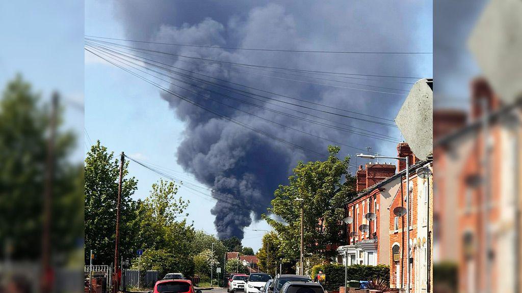 A plume of black smoke viewed from a residential street nearby