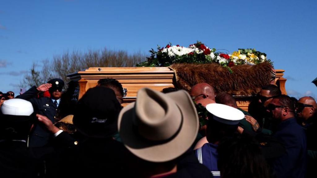 Onlookers watch and salute a coffin draped in furs being carried by pall bearers