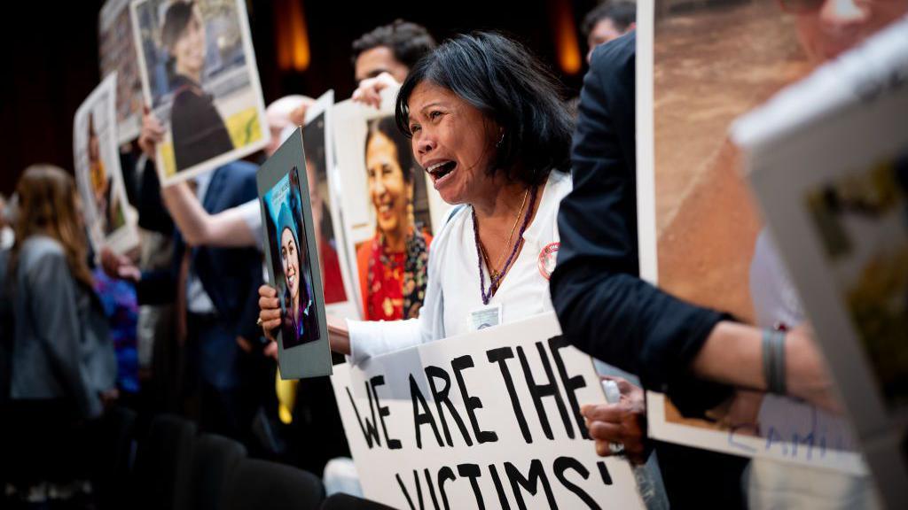 The mother of Danielle Moore cries, while holding a photograph of her daughter and standing with other family members of those killed in the Ethiopian Airlines Flight 302 and Lion Air Flight 610 at a congressional hearing in Washington with the head of Boeing in June 2024.