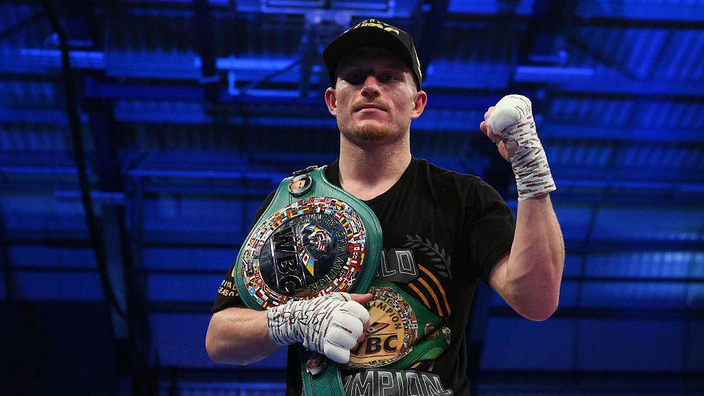 Dalton Smith poses in a dark baseball cap after a win, with a raised left fist and a title belt over his right shoulder