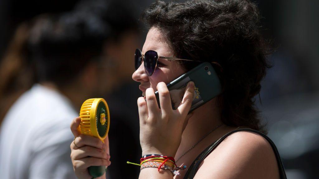 Woman talks on phone holding a yellow fan