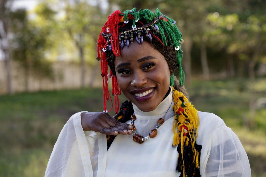 A woman wearing a tasselled red, green and yellow headdress smiles.