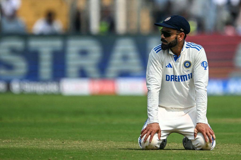 Virat Kohli sitting on the grass of a cricket field