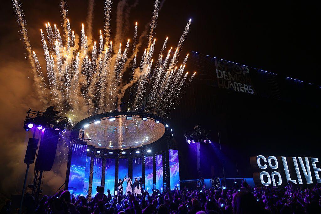 A crowd with their hands in the air watch performers on a stage in front of the Coop Live arena while fireworks go off in the sky 