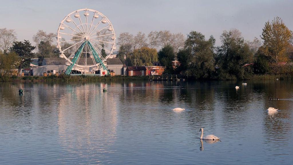 Lake and Ferris Wheel at Billing Aquadrome on a clear and calm autumn day. Waterfowl including swans are swimming on the lake.
