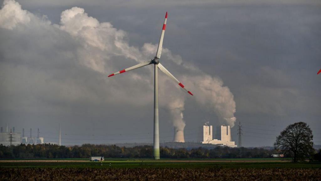 Wind turbine with power station in background