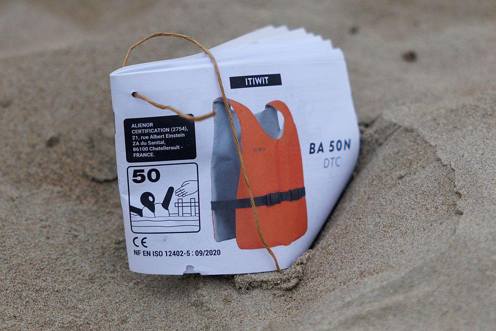 A discarded instruction manual for a life jacket lies on the sand
