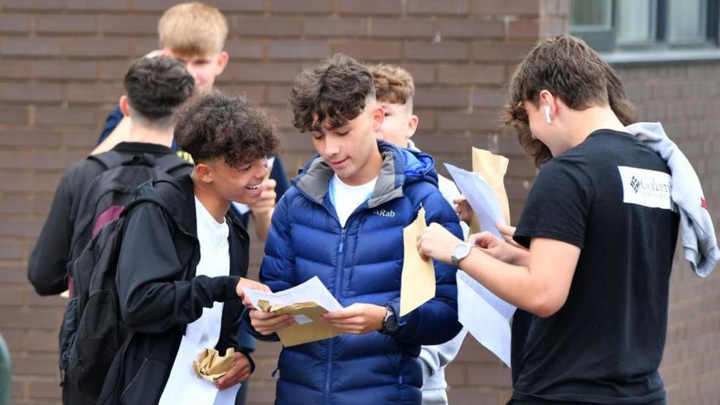 A group of boys opening envelopes outside a school.