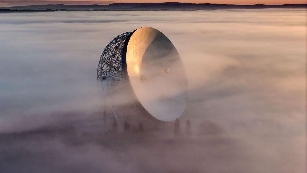 his aerial view the Lovell Telescope at Jodrell Bank emerges above morning fog at sunrise