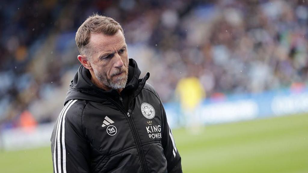 Gary Rowett, wearing a black tracksuit with Leicester branding, looks dejected on the pitch after a defeat