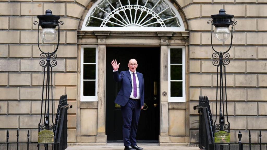Swinney waves to media outside Bute House