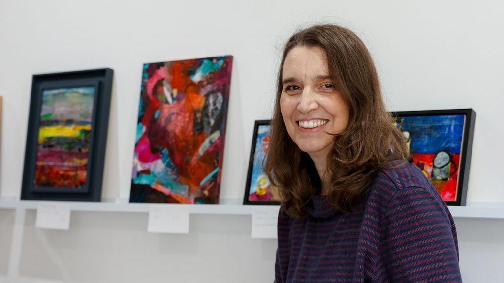 A local artist smiling at the camera exhibiting her artwork at the Royal United Hospitals (RUH) in Bath 