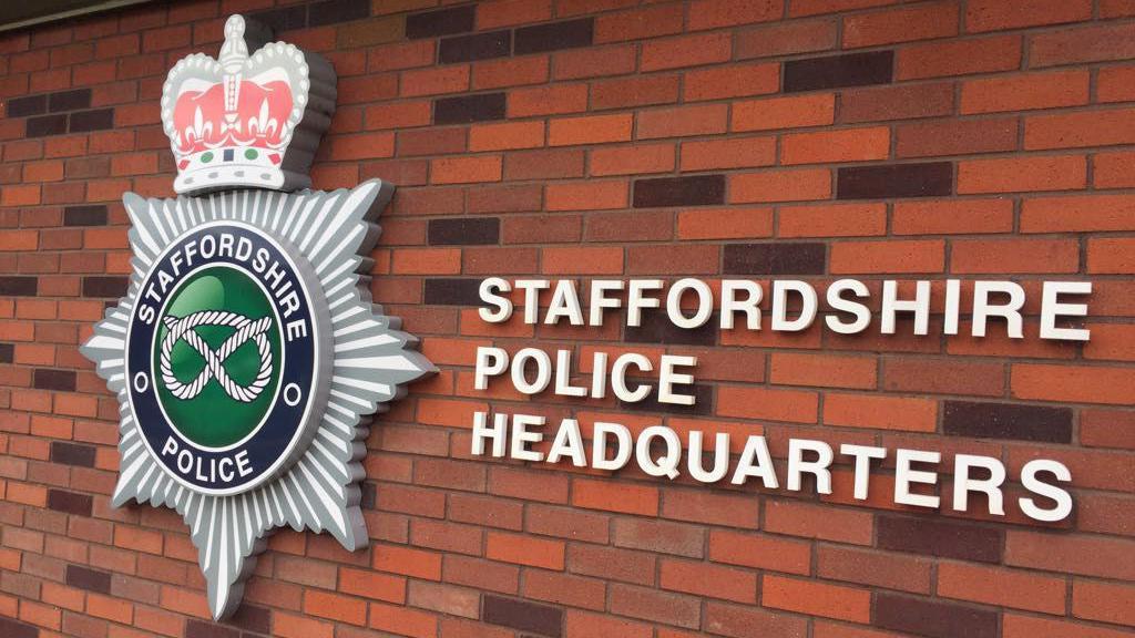 A sign at the headquarters of Staffordshire Police showing the police force's emblem and lettering to indicate it is the force's headquarters. They are on a red brick wall and the letters are in white with the police force's badge in red, white, grey, blue and green.