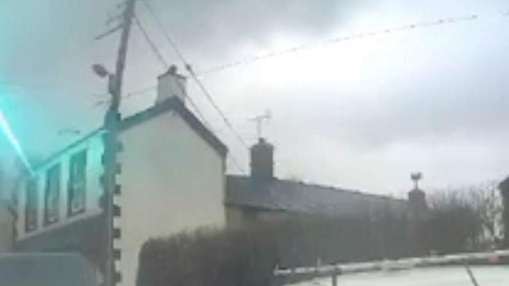 A flash of lightning hits the roof of a white house on a street.