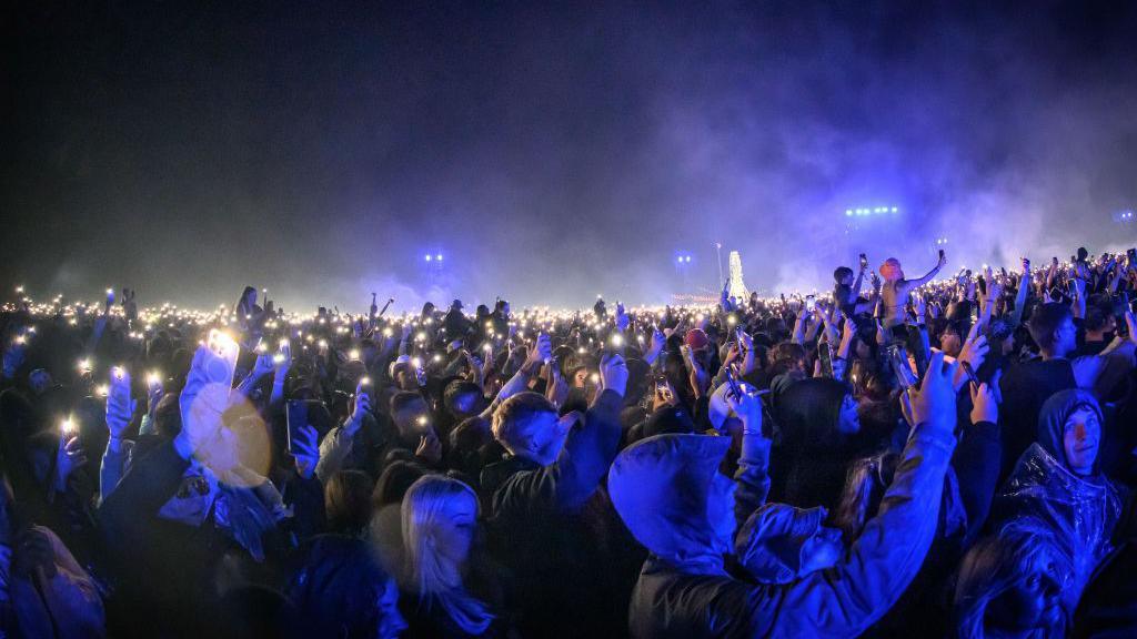A crowd of people at night lit up in blue light from a stage.
