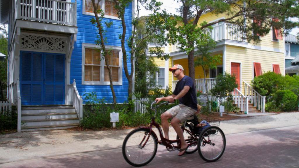 Man on bike going past colourful buildings in town of Seaside, Florida