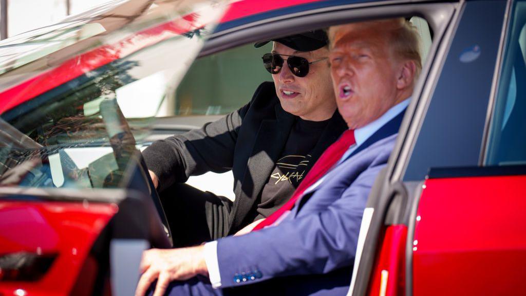 Trump and Musk sitting in a red Tesla with the door open, Trump in the driver's seat