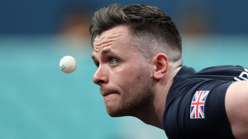 Aaron McKibbin looking at a table tennis ball while it is in the air