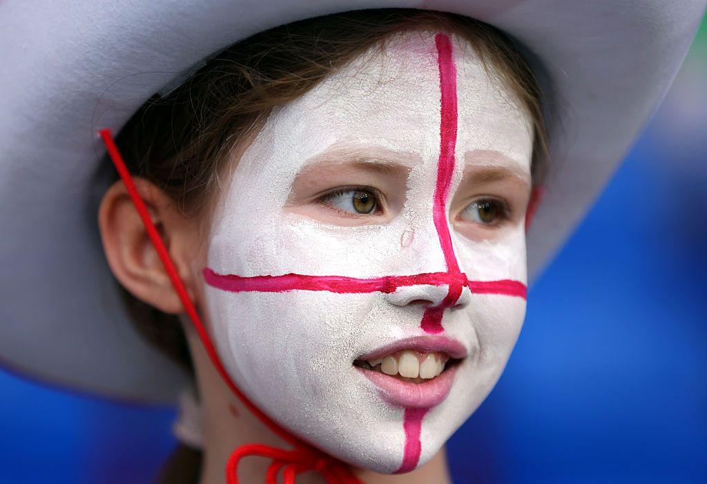 A girl wears a cowboy hat and smiles with her face painted white with a red cross