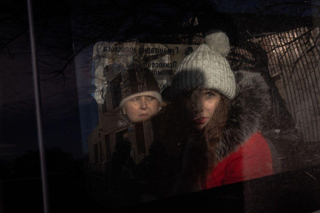 Two women, both wearing hats and warm coats, look out from the window of a car