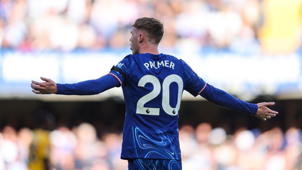 Cole Palmer celebrating on the pitch with his arms stretched out 