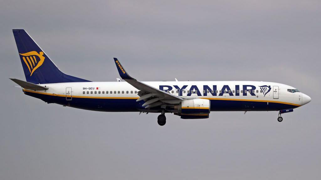 A Ryanair plane with white, blue and gold livery in mid-flight 