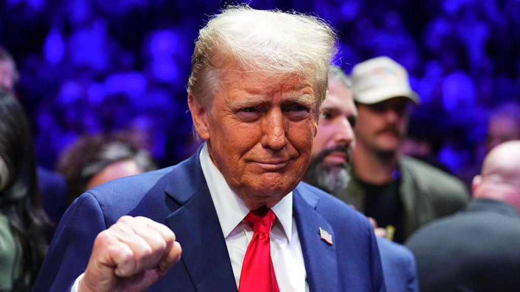 Donald Trump wearing a blue suit and red tie, pumps his fist in the air