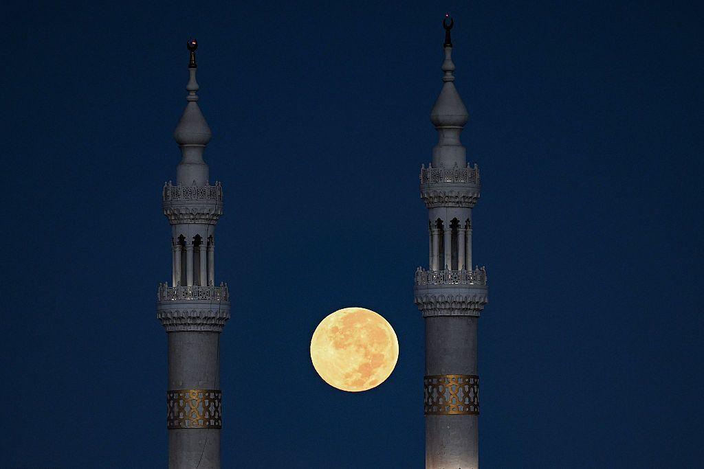 The full moon is visible between two towers.