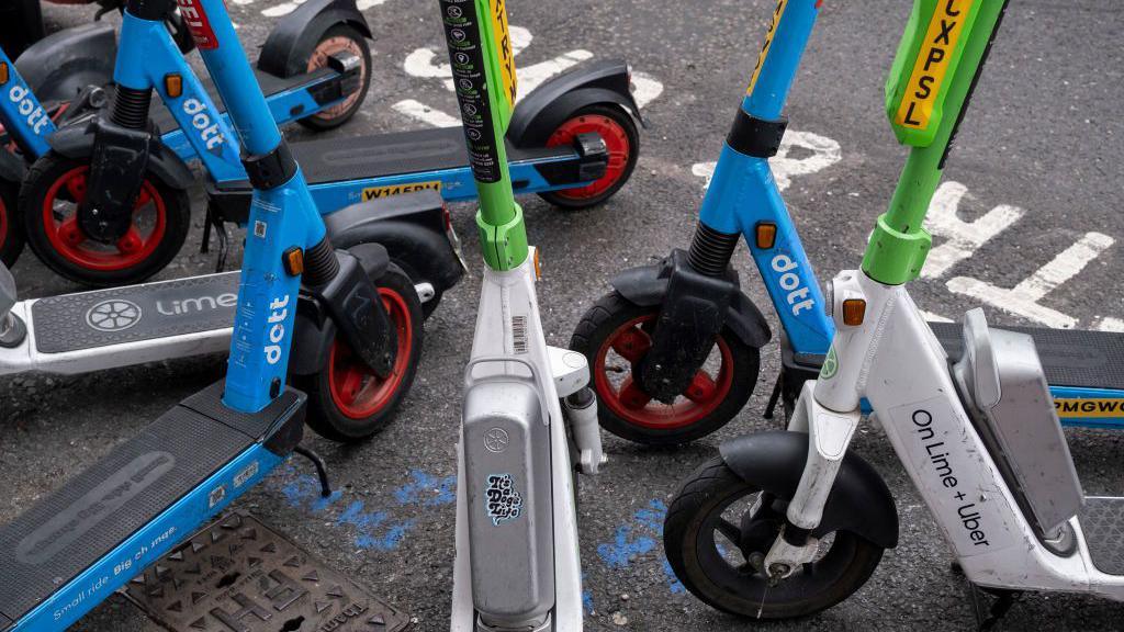 Cropped picture of several branded e-scooters parked on the side of the road