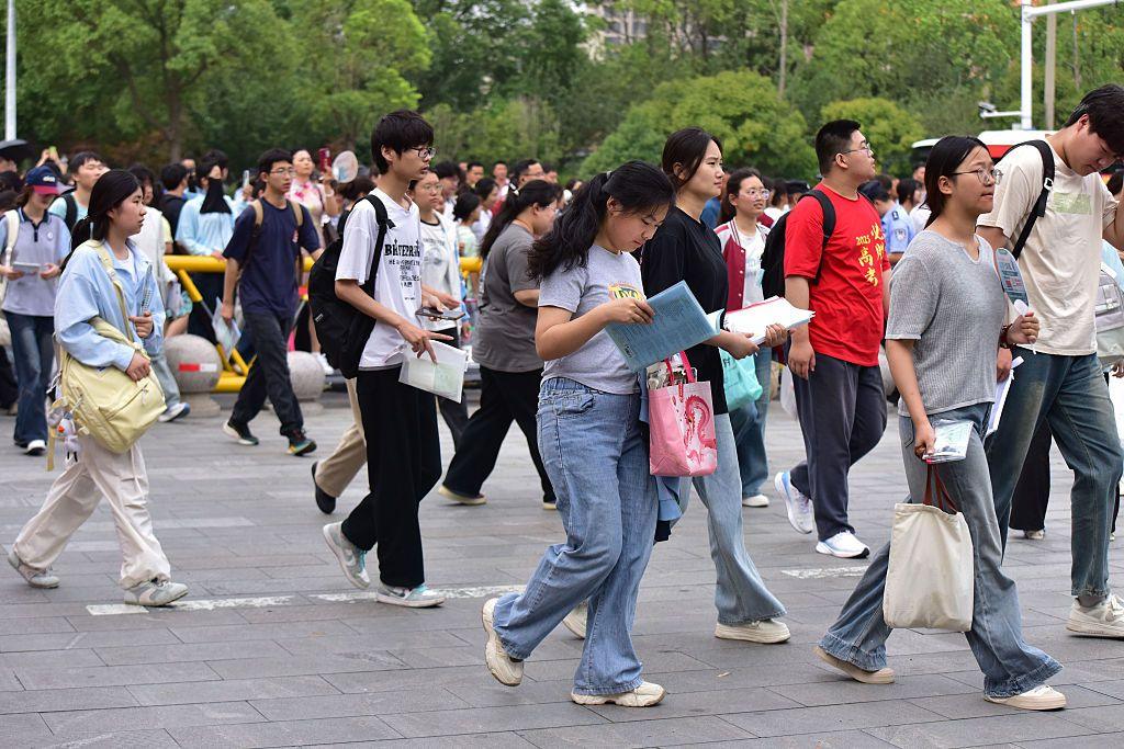 A girl reads a book while she walks with a dozen high school graduates into an exam venue for Gaokao this year