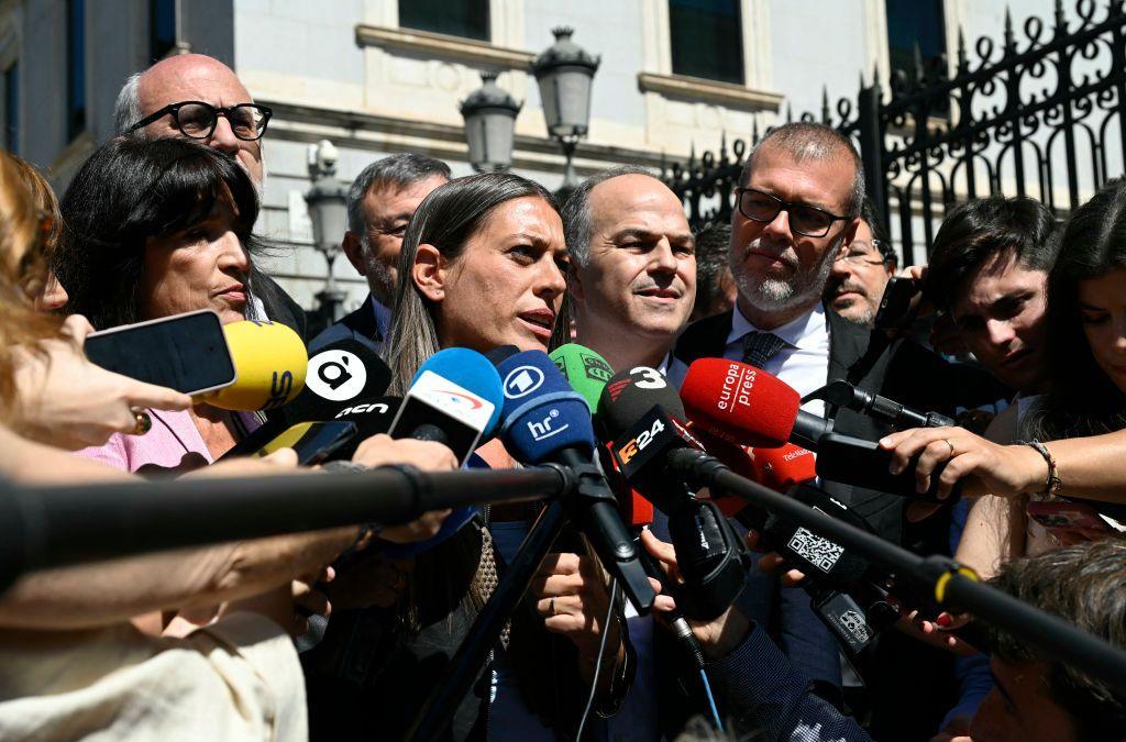 Miriam Nogueras standing in front of dozens of microphones surrounded by her colleagues