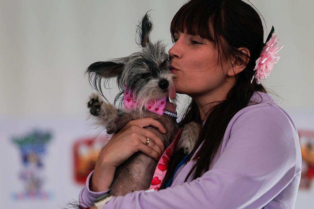 A woman in a purple top kisses a dog on the side of its head