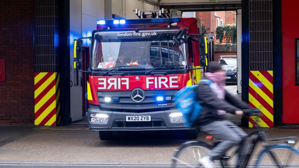 Fire engine leaving the fire station, as a cyclist travels past