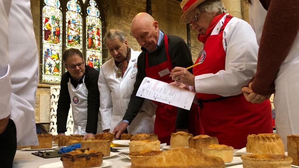 Men and women standing over a table filled with pies on paper plates