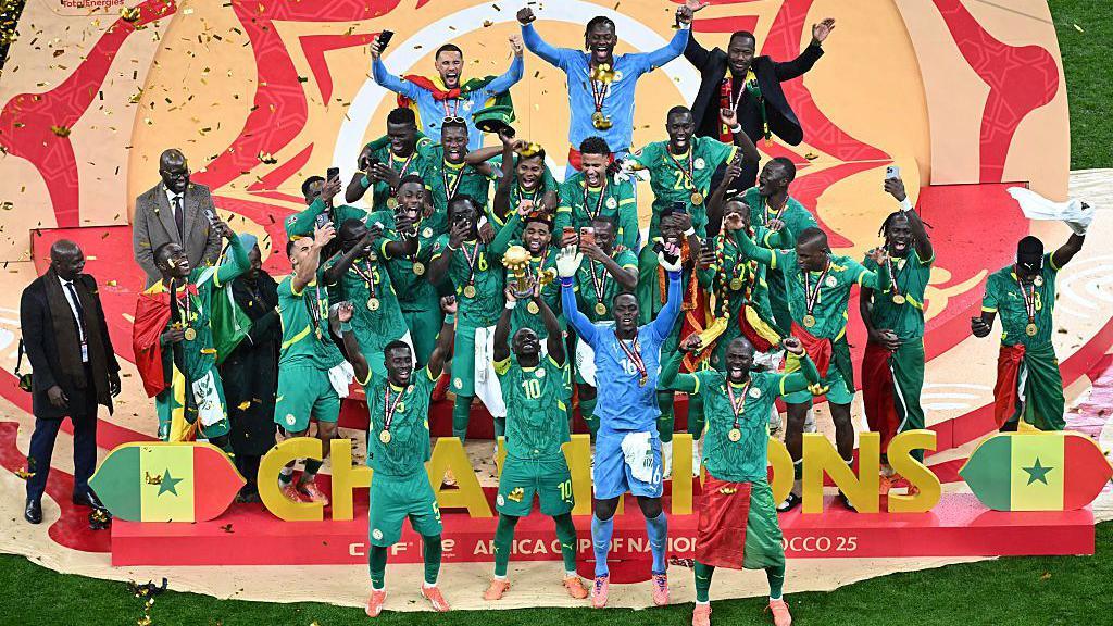 Senegal players celebrate after their win holding the trophy while confetti blows in the wind 