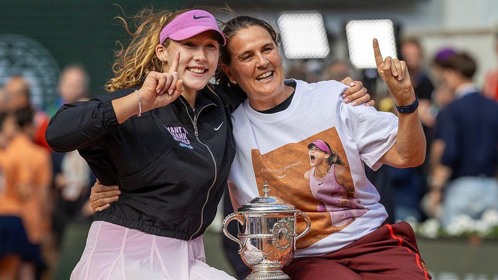 Mirra Andreeva and coach Conchita Martinez sit arm in arm and hold their index fingers to signify 'number one' with the French Open trophy between them