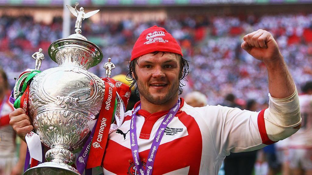 A close up of Keiron Cunningham hold the Challenge Cup in his right hand and punching the air with his left